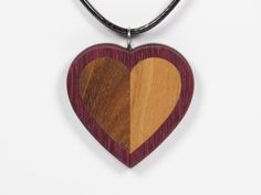 A wooden heart pendant made from afromosia (brown) and cherry (orange beige) inlaid in purpleheart (purple). The pendant is sanded smooth and finished with Danish Oil to bring out the grain of the wood and to add protection. The eyelet is made of stainless steel. The pendant is 1 5/8 Handmade Brown Heart Pendant Necklace, Heart-shaped Brown Necklace For Gift, Brown Heart Shaped Jewelry With Heart Beads, Brown Heart-shaped Necklace For Gift, Brown Heart Charm Necklace As Gift, Brown Heart Charm Necklace As A Gift, Brown Heart Charm Necklace For Gift, Brown Necklace With Heart Charm For Gift, Brown Heart-shaped Necklace For Valentine's Day