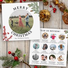 two christmas cards sitting on top of a wooden table next to pine cones and evergreens