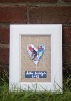 a white frame with a heart cut out of it sitting in the grass next to a brick wall