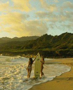 two women are walking into the ocean with a surfboard