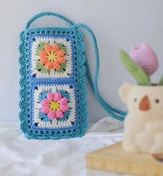 a crocheted purse sitting on top of a bed next to a teddy bear