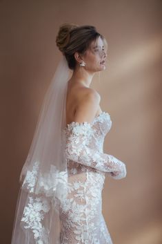 a woman in a wedding dress with a veil on her head and one arm over her shoulder