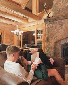 a man and woman sitting on a couch in front of a fire place reading books