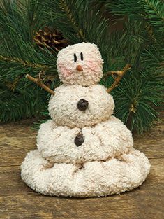 a snowman made out of yarn sitting on top of a wooden table next to a pine tree