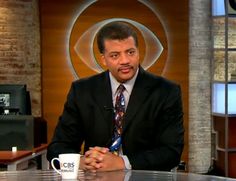 a man in a suit and tie sitting at a table with a cup on it