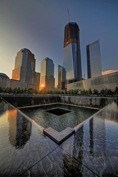 the sun is setting behind skyscrapers and reflecting in water on a sunny day with no clouds