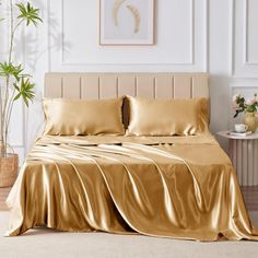 a bed with gold sheets and pillows in a white room next to a potted plant