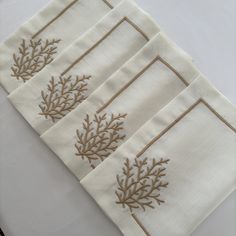 four napkins with embroidered designs on them sitting on a white tablecloth covered table