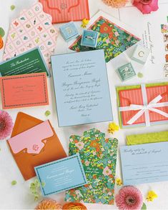 many different types of wedding stationery and envelopes on a table with flowers in the background