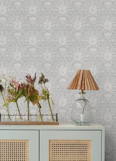 two vases with flowers sitting on top of a white cabinet next to a lamp