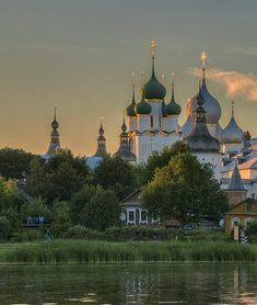 a large white building with green domes sitting on top of a lush green field next to a lake