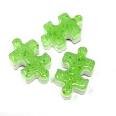 three pieces of green and white glittered plastic puzzle pieces on a white table top