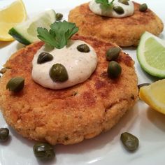 two crab cakes on a plate with lemons and capers