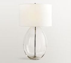 a clear glass table lamp with a white shade on the base and a light bulb attached to it