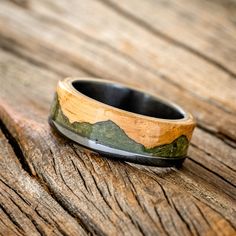 a wooden ring with mountains on it sitting on a piece of wood that has been carved