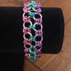 a colorful bracelet is on display on a black velvet stand with a wooden table in the background