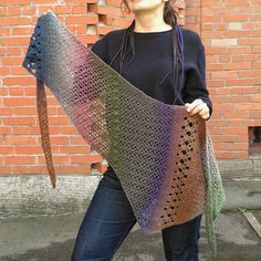 a woman holding up a crocheted shawl in front of a brick wall