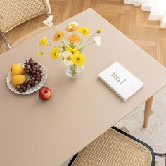 a table with flowers and fruit on it in front of a book sitting on a chair