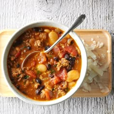 a white bowl filled with chili and beans on top of a cutting board next to rice