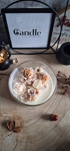 a glass bowl filled with cream and flowers on top of a wooden table next to an empty candle holder