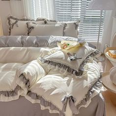 a bed with white sheets and ruffles on it in front of a window