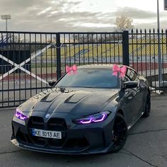 a black sports car with pink bows on it's hood parked in front of a gate