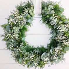 a wreath is hanging on the wall with greenery and white flowers around it,