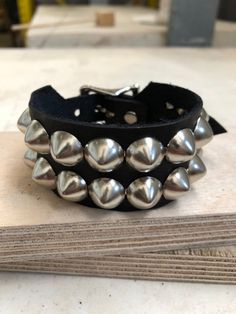 Classic studded punk bracelet with 2 rows of 1/2" cone studs. Fastens with a buckle and is adjustable. All hardware is nickle plated.Studs on black bracelets are nickel plated brass, studs on colored bracelets are nickel plated steel (old stock)Smaller bracelets have fewer studs per row.Made with hand dyed vegetable tan leather.Note: red bracelet is kind of pink-ish.Bracelet is 1.25" wide.Ask about custom sizing and color options! Punk Adjustable Cuff Bracelet With Rivets, Adjustable Punk Cuff Bracelet With Rivets, Punk Style Adjustable Cuff Bracelet With Rivets, Metal Spiked Leather Bracelet For Parties, Punk Black Bracelet With Silver Studs, Silver Rivets Wristband For Concert, Adjustable Spiked Leather Bracelet For Parties, Gothic Metal Bracelets With Spikes, Adjustable Metal Cuff Bracelet In Punk Style