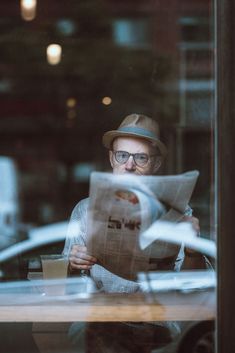 a man reading a newspaper while sitting at a table in front of a glass window