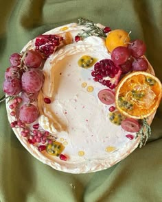 a cake decorated with grapes and oranges on a green tablecloth, next to an orange slice