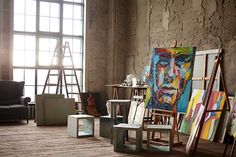 an artist's studio with easels and paintings on the floor in front of large windows