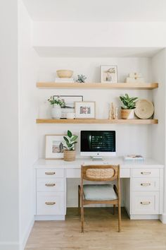 a desk with a computer and some plants on top of it in front of shelves