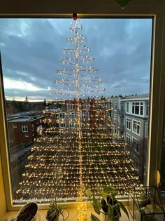 a christmas tree made out of lights in front of a window with a view of the city