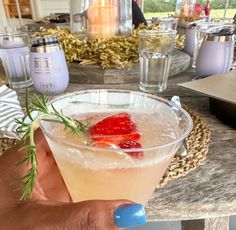 a person holding up a drink with strawberries on the rim and garnish