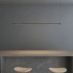 two white stools sitting at a table in front of a gray wall with an overhead light