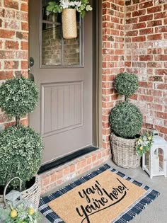 two potted plants are sitting on the front door mat that says, you're here