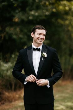 a man in a tuxedo smiles as he poses for the camera with his hands on his hips