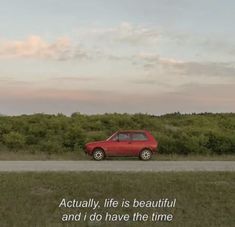 a red car parked on the side of a road next to a lush green field