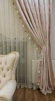 a white chair sitting in front of a window next to a curtain with tassels on it