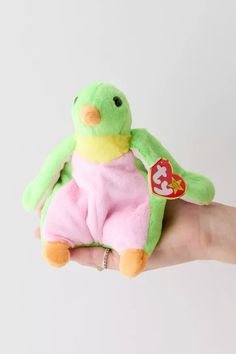 a hand holding a small green and pink stuffed animal with a tag on it's chest