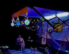 a woman sitting on a chair in front of a trailer with christmas lights hanging from it