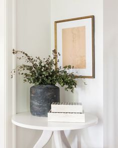 a small white table with a vase on it and a book sitting on top of it