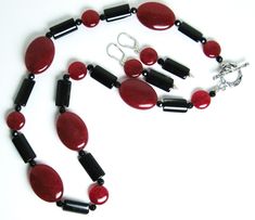 Red mountain jade, black tourmaline necklace (19 inches) with a sterling silver toggle clasp. The matching earrings are on sterling silver leverbacks with a 1.4-inch drop. Red mountain jade is a gemstone of color-enhanced high-grade dolomite marble from Asia. Both red mountain jade and tourmaline are gemstones. There are two shapes of red mountain jade beads: flattened ovals (25 x 18 mm) and flattened round beads (11 mm in diameter).The black tourmaline beads are flattened cylinders (16 x 9 mm).There are also 4 mm black faceted beads in the necklace. Red mountain jade is the gemstone of October-November. Tourmaline is a birthstone of October. Classic Pendant Jewelry With Lobster Clasp, Formal Jade Jewelry With Round Beads, Elegant Onyx Dangle Jewelry, Adjustable Costume Jewelry With Lobster Clasp, Adjustable Red Formal Jewelry, Oval Jade Gemstone Beads Jewelry, Sterling Silver Round Beads Fine Jewelry, Oval Jade Jewelry With Natural Stones, Sterling Silver Single Strand Round Jewelry