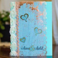 a blue and gold wedding card with two hearts on the front, sitting on a table