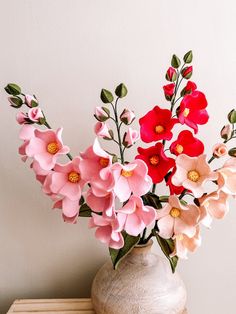 a vase filled with pink and red flowers on top of a wooden table next to a white wall