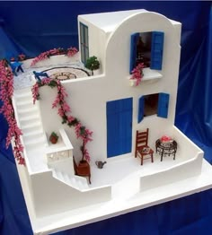 a model of a house with blue shutters and flowers on the windows, stairs and tables