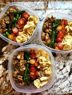 three plastic containers filled with pasta and veggies on top of a marble counter