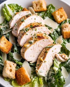 a white bowl filled with meat and greens on top of a table next to bread