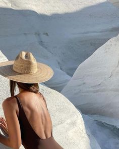 a woman in a brown swimsuit and straw hat sitting on some white rock formations