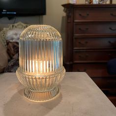 a clear glass lamp sitting on top of a table next to a dresser and chair